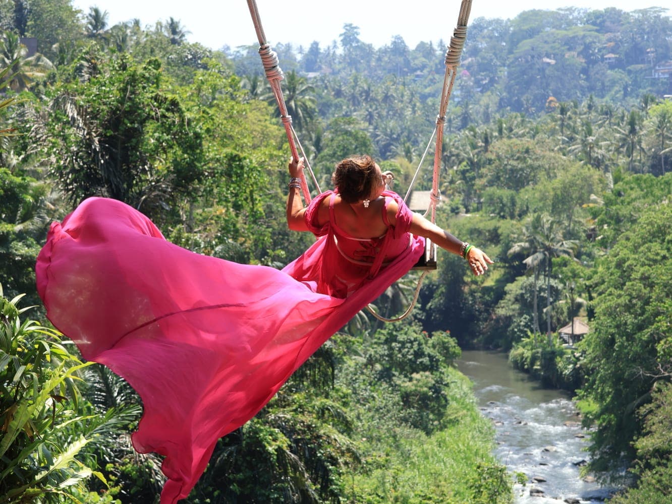Gast van Edi in een roze jurk op de Bali Swing, hoog boven de jungle en de rivier bij Ubud
